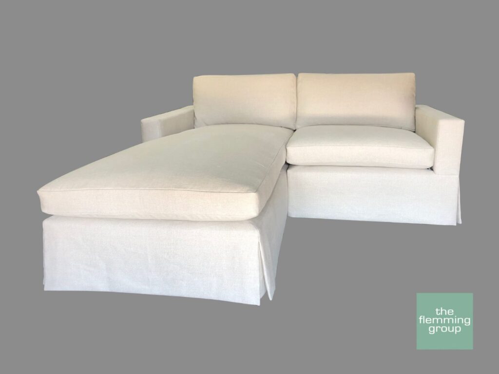 A white couch with two pillows and one ottoman.